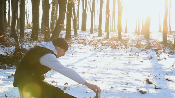 Hombre joven haciendo ejercicios de estiramiento durante el entrenamiento de invierno al aire libre en clima frío en el parque. Árboles en la nieve. Clima nieve y sol. Fitness en la calle en invierno — Vídeos de Stock