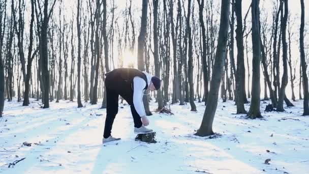Чоловік зав'язує взуття для бігу в лісі. Зимові тренування в сонячний день — стокове відео