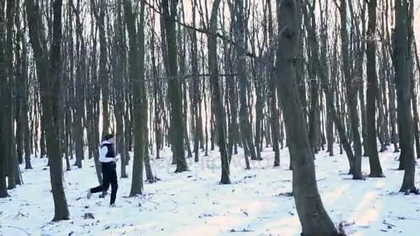 Ziemlich athletischer Typ, der im Winter im Wald läuft und bei Sonnenuntergang Musik mit Kopfhörern hört — Stockvideo