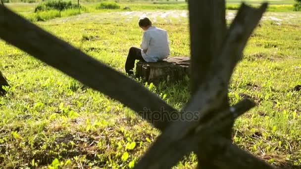 Kleine man zit op een boomstronk en tekenen van een landschap — Stockvideo
