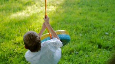 Zavallı çocuk bir salıncak bir lastik, sürme güzel bir arka plan yeşil çim bahçesinde boyalı. Ağır çekim
