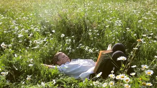 Парень лежит на траве и читает книгу — стоковое видео