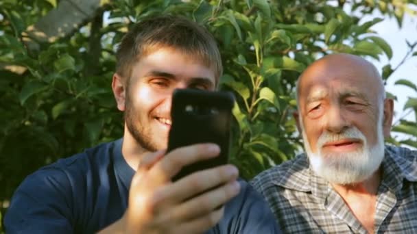 Dwie osoby Brodaty mówić za pośrednictwem wideorozmowami smartphone siedząc w parku — Wideo stockowe