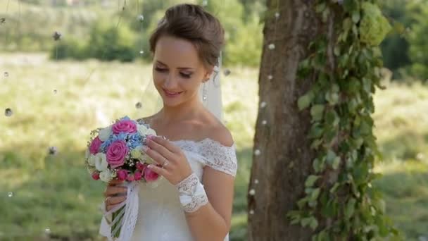 Mooie bruid in een witte jurk met een boeket in het park — Stockvideo