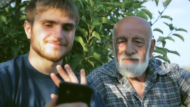 Двоє фермерів проводять відеоконференцію зі смартфоном, що сидить у саду — стокове відео