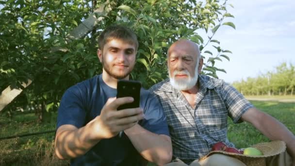 Apariencia en el pueblo de Internet de buena calidad. Un nieto con un abuelo habla a través de una videollamada usando un teléfono inteligente — Vídeos de Stock