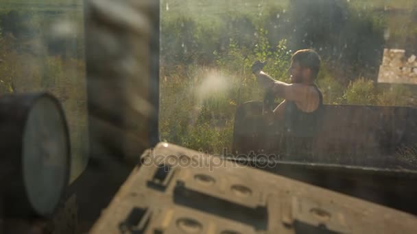 A man makes a warm-up before training at the abandoned construction site. Shot through a dirty window — Stock Video