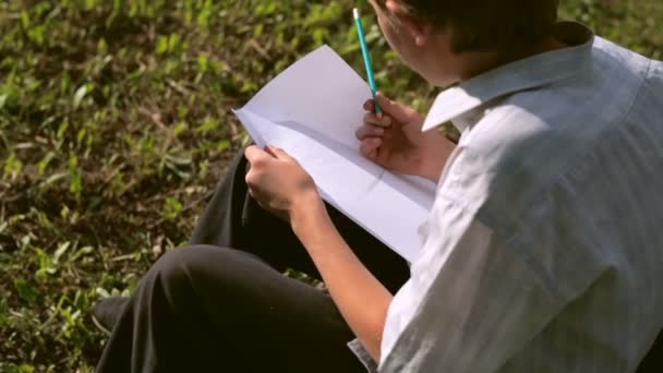 Um menino desenha um projeto no papel — Vídeo de Stock