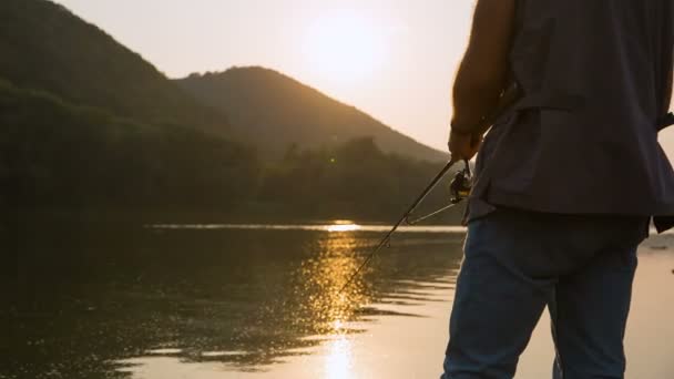 Рука с прялкой и катушкой на вечернем летнем озере — стоковое видео