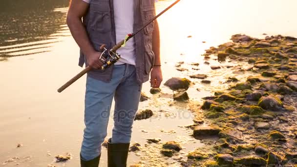 Un joven cerca del río en una noche de verano. Pescador feliz al atardecer — Vídeo de stock