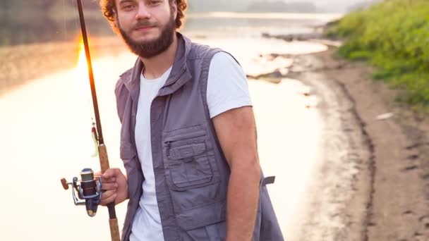 Um jovem pescador mostra um gosto e sorri. Pescador feliz ao pôr do sol — Vídeo de Stock