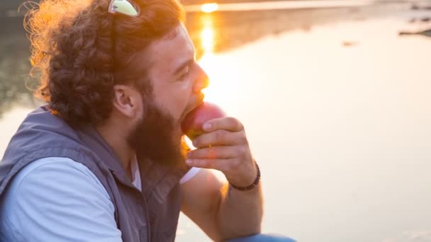 Красивый хипстер кусает яблоко на закате — стоковое видео