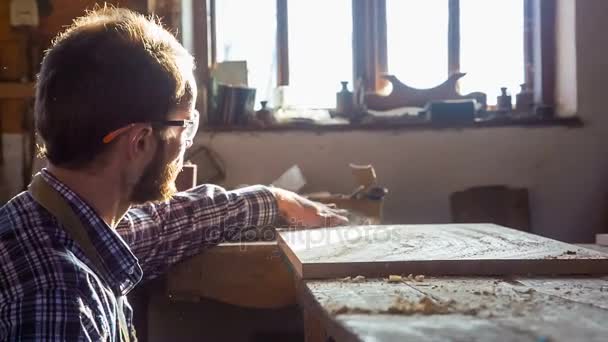 年轻的木匠选择一块覆盖着碎屑和灰尘的木板。已成为企业的爱好 — 图库视频影像