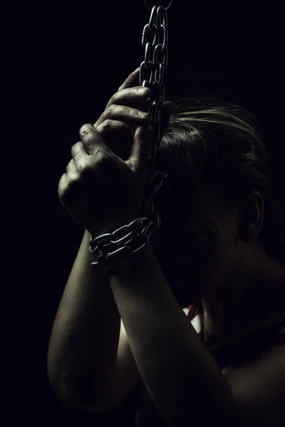 Mão das mulheres brancas estão no chão acorrentadas correntes de metal close-up em um fundo preto, tonificado para um filme retro — Fotografia de Stock