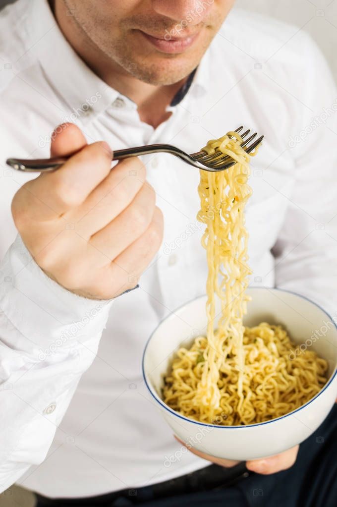 Young man is eating instant noodles from the white bowl