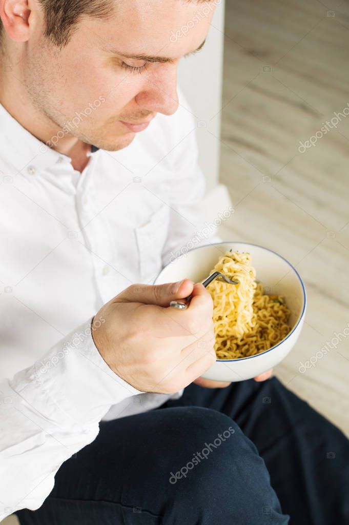 Young man is eating instant noodles from the white bowl