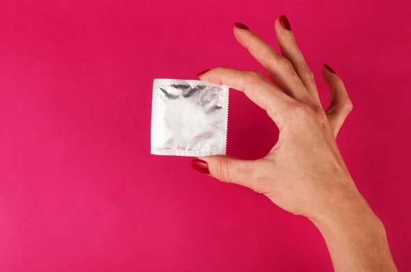 Mujer sosteniendo condón sobre el fondo rosa. Concepto de protección sexual — Foto de Stock