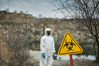 Koruyucu tulumlu bir kız. Biyolojik koruma giysisi, yüzünde maske ve gözlük. Virüsün bulaşmasını önlemek için kişisel koruyucu ekipman. Koronavirüs, salgın, grip ve karantina kavramı. Biyolojik tehlike sembolü.