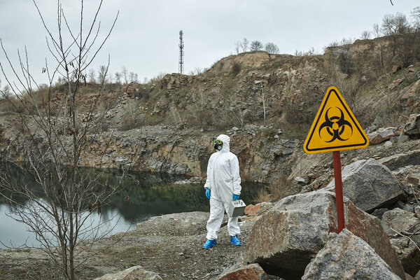 Girl in protective overalls on the nature. Biological protection suit, mask and glasses on the face. Personal protective equipment to prevent transmission of the virus. The concept of coronavirus, pandemic, flu and quarantine. Symbol of biohazard.