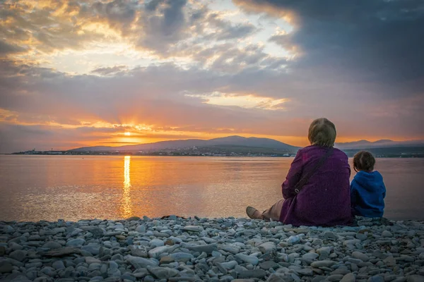 Бабуся і внучка, дивлячись на захід сонця на березі затоки Ліцензійні Стокові Зображення