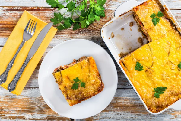 Portion of delicious moussaka on plate and in gratin dish — Stock Photo, Image