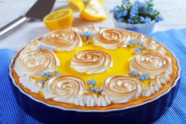 Classic french lemon tart - crisp pastry with a smooth lemon filling decorated with meringue roses and edible fresh flowers, view from above, close-up