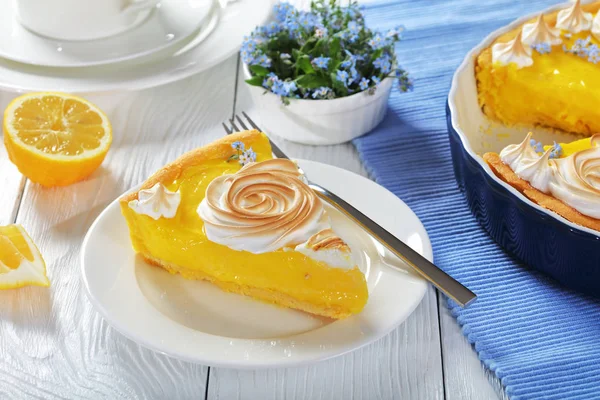 slice of Classic french lemon tart - crisp pastry with a smooth lemon filling decorated with meringue roses and edible fresh flowers, close-up