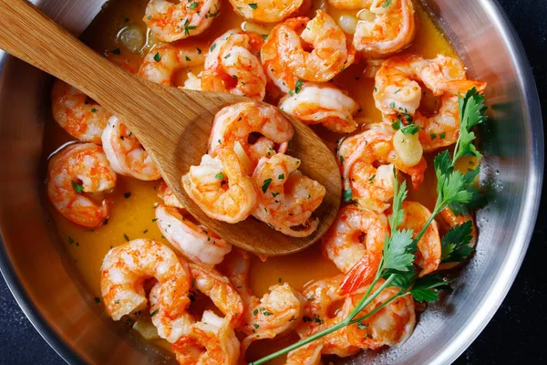Italian shrimp scampi with garlic butter sauce served with lemon and parsley, on a skillet on concrete background, top view, horizontal orientation, close-up