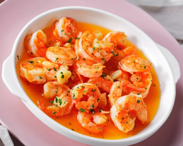 Garlic and butter shrimp scampi sprinkled with parsley served on a pink plate on white wooden background, horizontal orientation, close-up