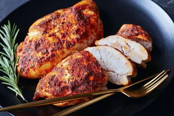 スパイシーな焼きたての鶏の胸は 黄金のカトラリーと新鮮なローズマリーの小枝と黒プレート上で提供 水平方向 クローズアップ — ストック写真