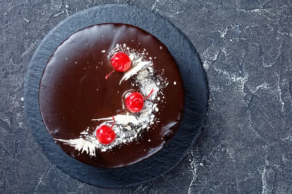 Chocolate and cherry cake with cherry pie filling topped with chocolate glaze decorated with white chocolate and canned cherries served on a dark concrete background, top view, flat lay