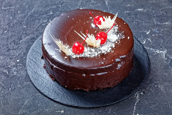 Devil\'s chocolate and cherries cake with cherry pie filling with dark chocolate glaze decorated with white chocolate and canned cherries on top served on the concrete table, close-up