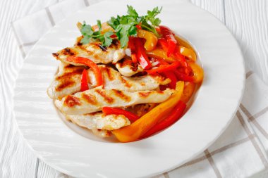 Close-up on a white plate with weight loss meal of grilled chicken steaks with stir fry sweet pepper strips, fresh parsley on top and green herb sauce on a white plate on a wooden background clipart