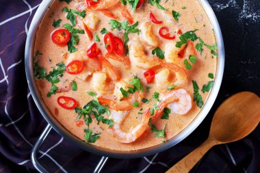 close-up of Tom Yum soup, tom kha soup in a saucepan on a concrete table with brown cloth and spoon, horizontal view from above, flat lay clipart