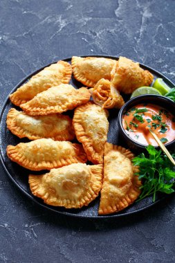 vertical view of hot deep-fried Buffalo Chicken Empanadas with Low-Calorie Dip on a black platter on a concrete table, horizontal view from above clipart