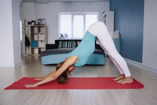 Woman practicing yoga, downward facing dog pose indoor — ストック写真