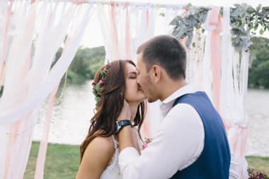 arka plan dekorasyon şeritler ve Gölü üzerinde açık havada beyaz bir gelinlikle çok güzel bir gelin mutlu damat koyu mavi elbiseli kisses