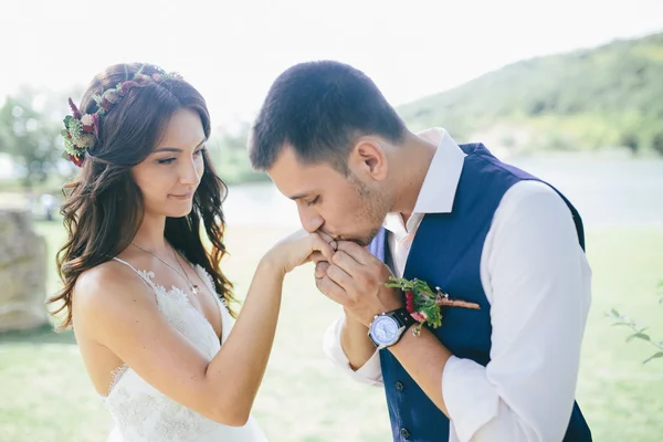 Sposo felice in un abito blu scuro bacia la mano della sua bella sposa in un abito da sposa bianco all'aperto. concentrarsi sulla sposa — Foto Stock