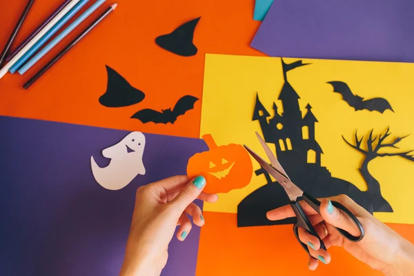 Közelről női kéz, olló vágja papír narancssárga sütőtök, a háttérben Halloween összetétele. Vár, szellemek, a denevérek, a sütőtök vágják, színes papír. Házi dekorációk, Halloween — Stock Fotó