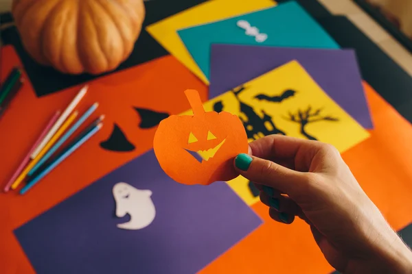 Mujer sostiene papel hecho a mano calabaza naranja en la composición de Halloween de fondo. Castillo, fantasmas, murciélagos, calabazas están en el fondo de papel artesanal de colores . — Foto de Stock