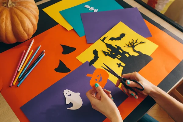 Cerrar las manos femeninas con tijeras calabaza de papel cortado en el fondo composición de Halloween . — Foto de Stock