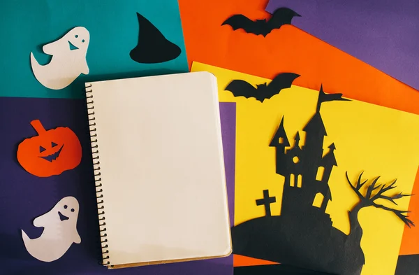 Halloween holiday background with blank notebook and castle, ghosts, bats, pumpkins cut black, yellow, purple, orange paper. top view