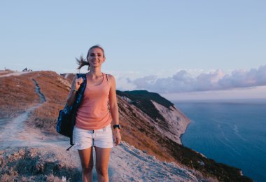 Arka plan deniz ve gün batımı gökyüzünde bir uçurumun kenarında yürüyen genç güzel sarışın kadın Portresi