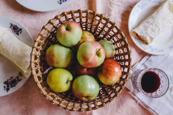 Ripe apples in wicker plate standing on a pink tablecloth next to the pita bread and grape juice — Stock Photo, Image