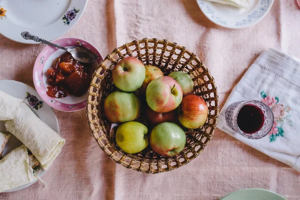 Ripe apples in wicker plate standing on a pink tablecloth next to the pita bread, apple jam and grape juice — Stock Photo, Image