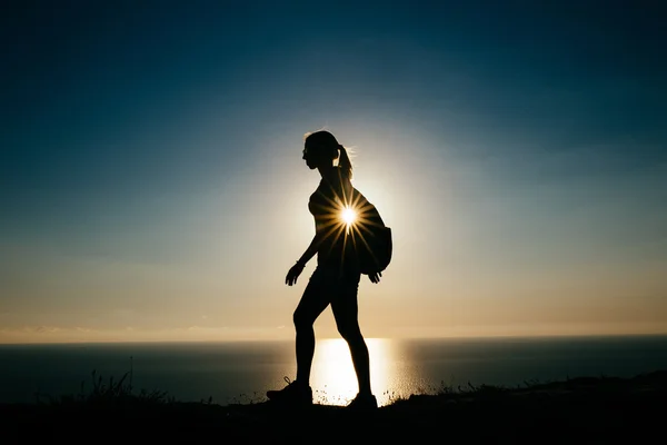 Silhouette Young woman tourist with backpack goes on the background on sunset sky and sea — Stock Photo, Image