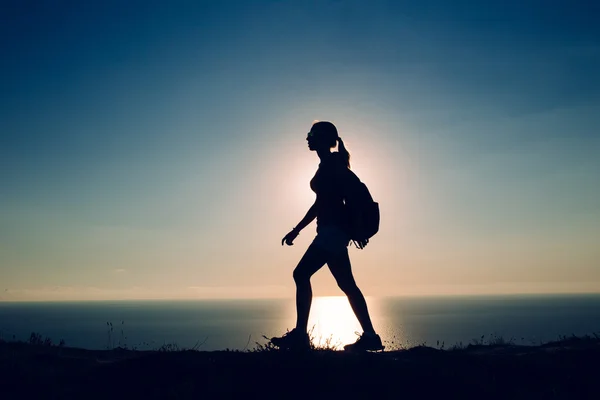 Silhouette Young woman tourist with backpack goes on the background on sunset sky and sea — Stock Photo, Image