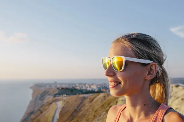 Портрет активной улыбающейся молодой женщины туристки в солнцезащитных очках на фоне горной вершины скалы и моря — стоковое фото