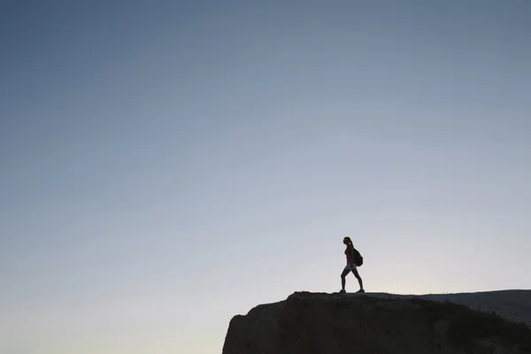 Silhuet ung kvinde turist med rygsæk stående på klippen - Stock-foto
