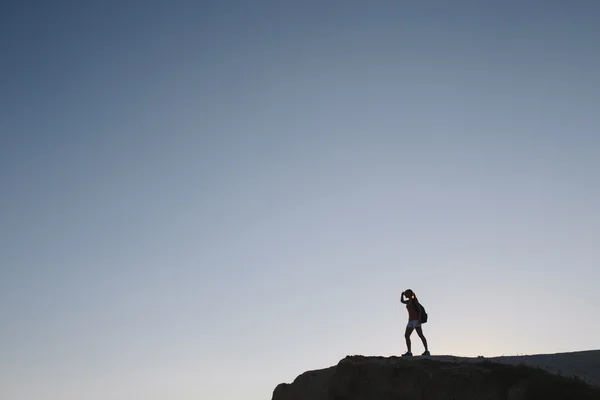 Silhouette young woman tourist with backpack standing on cliff — Stock Photo, Image